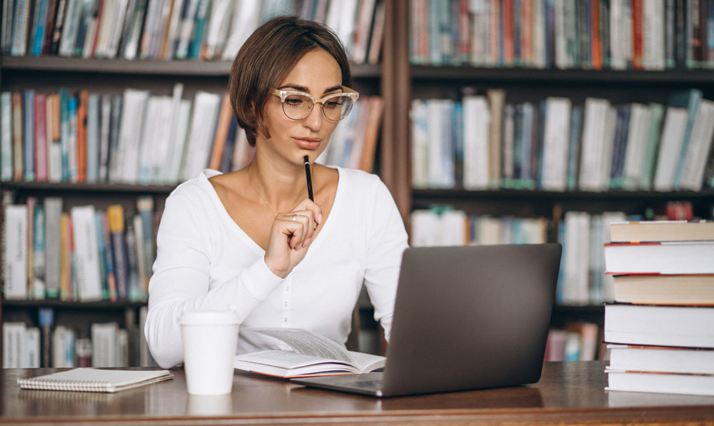 donna in biblioteca che studia e segue una lezione online